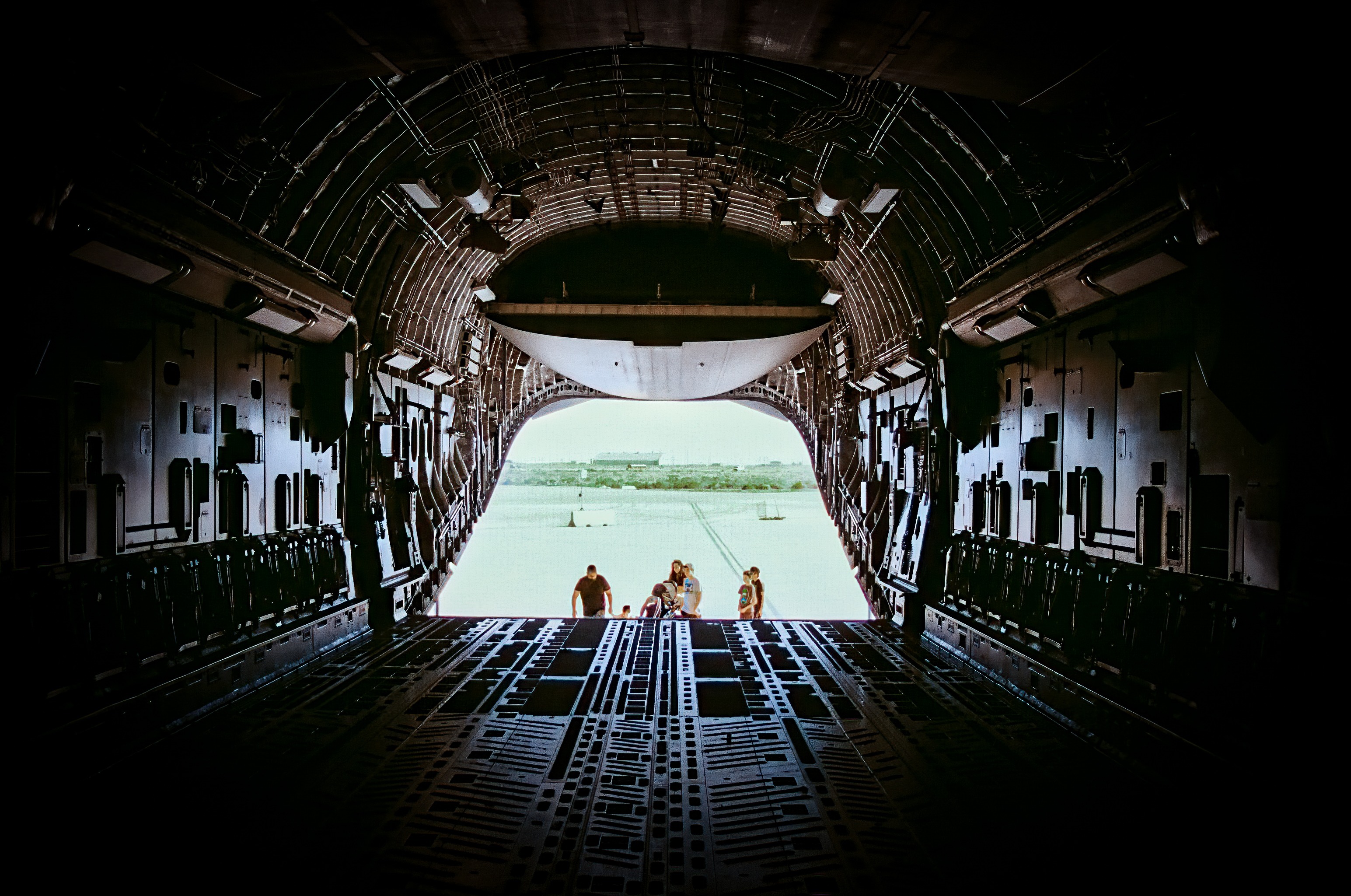 Interior of military cargo aircraft with personnel at open rear ramp
